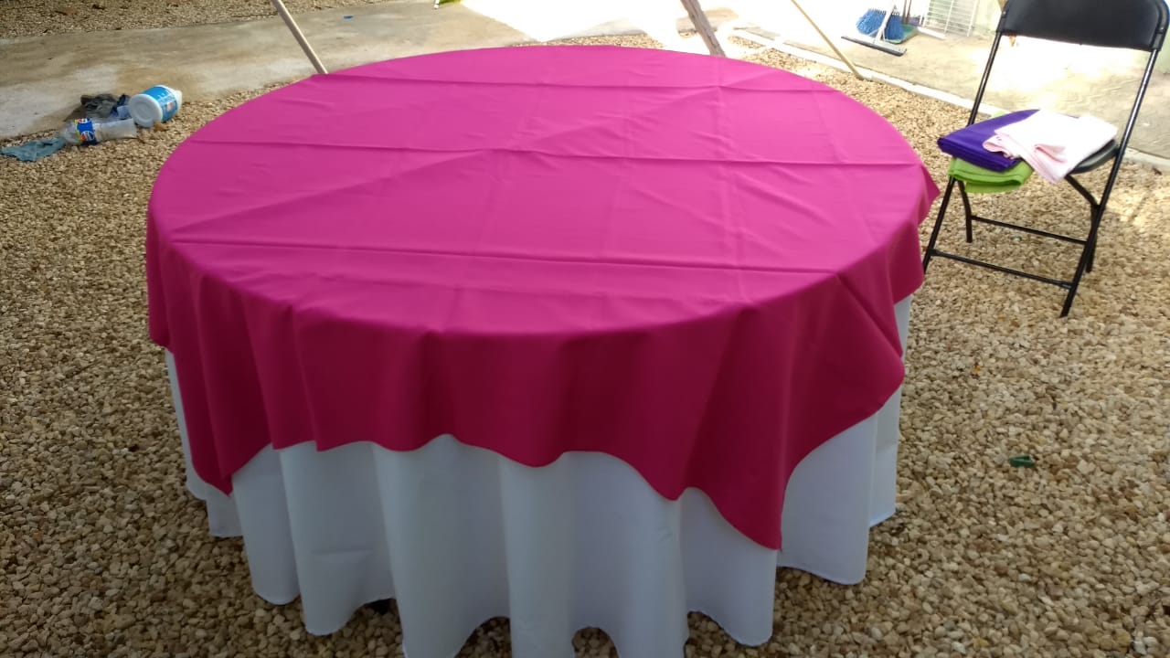 Mesa redonda con mantel blanco y cubremantel fucsia