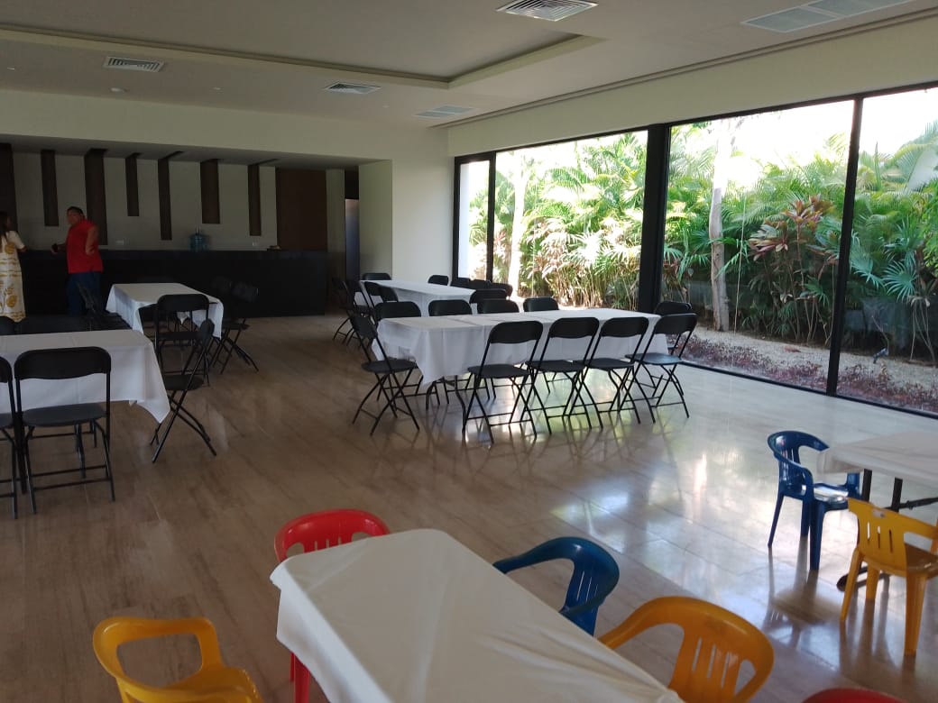 Salón con mesas largas cubiertas con mantel blanco y sillas plegables negras